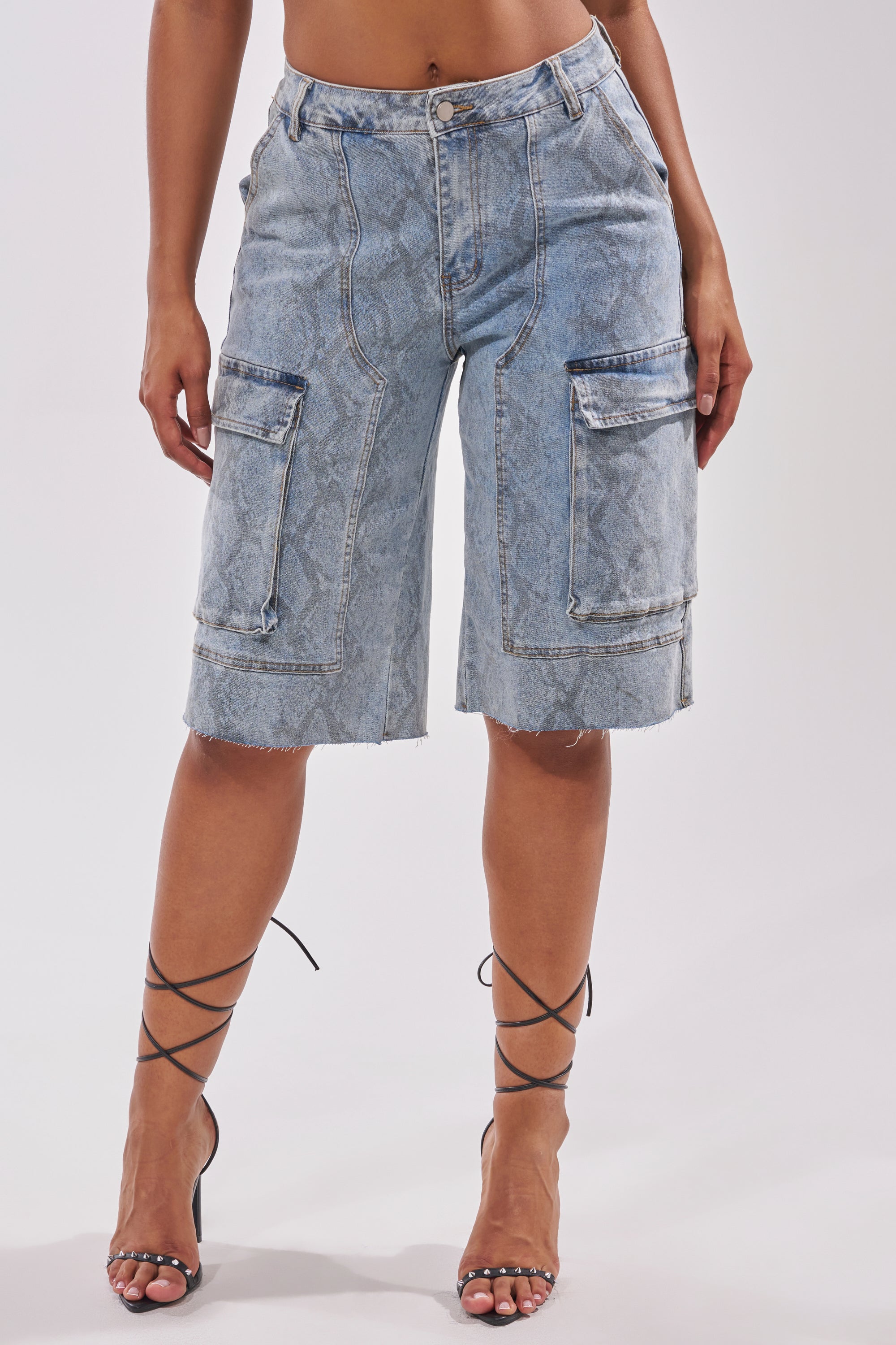 A person is wearing LITTLE SNAKE BERMUDA SHORTS—high-waisted, knee-length denim with front pockets and frayed hems—paired with black strappy heeled sandals. Upper body is not visible. 0