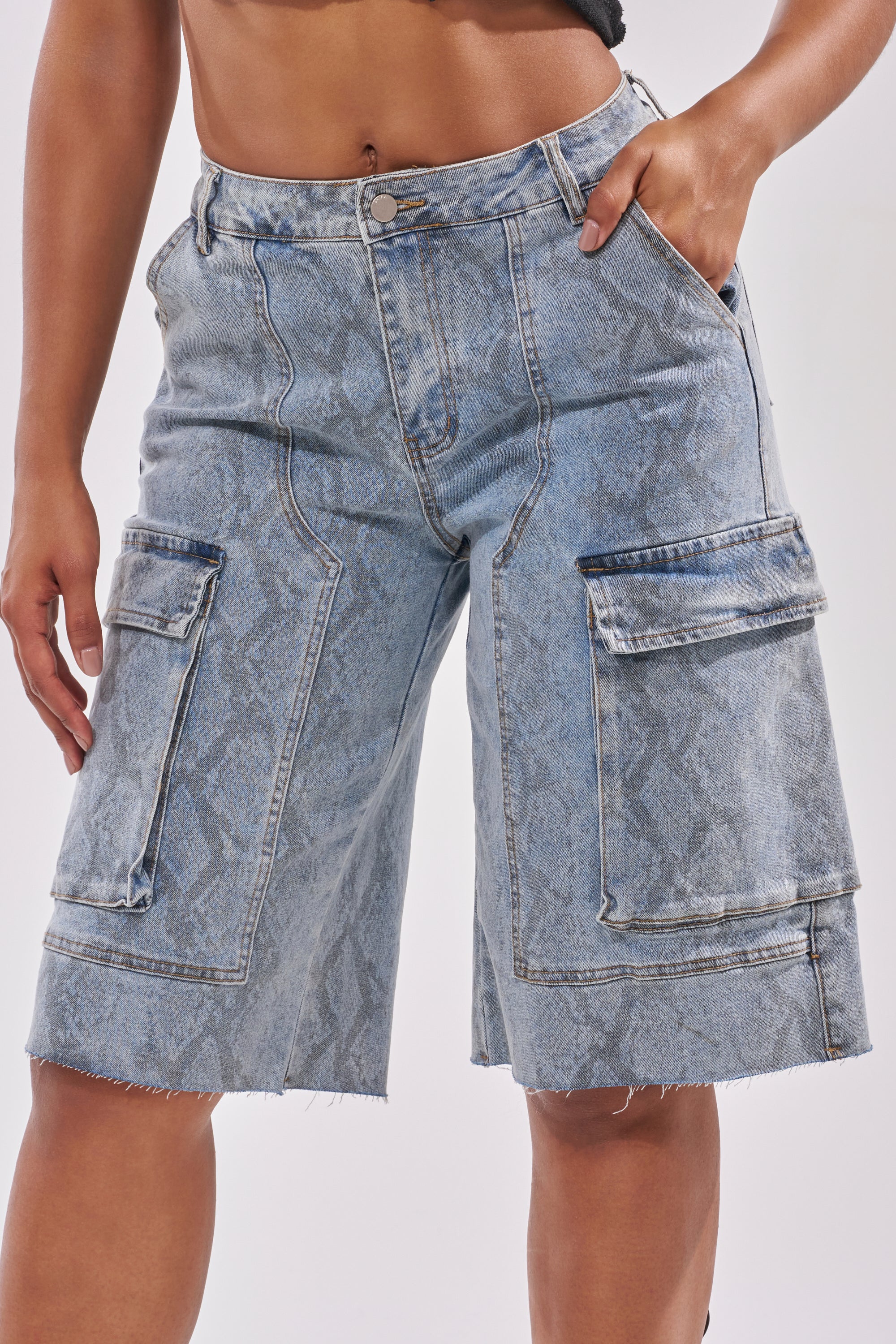 A person wearing the LITTLE SNAKE BERMUDA SHORT—high-rise, light wash denim bermuda shorts featuring a snake print, frayed hems, large side pockets, button fly—with one hand in their pocket. 5