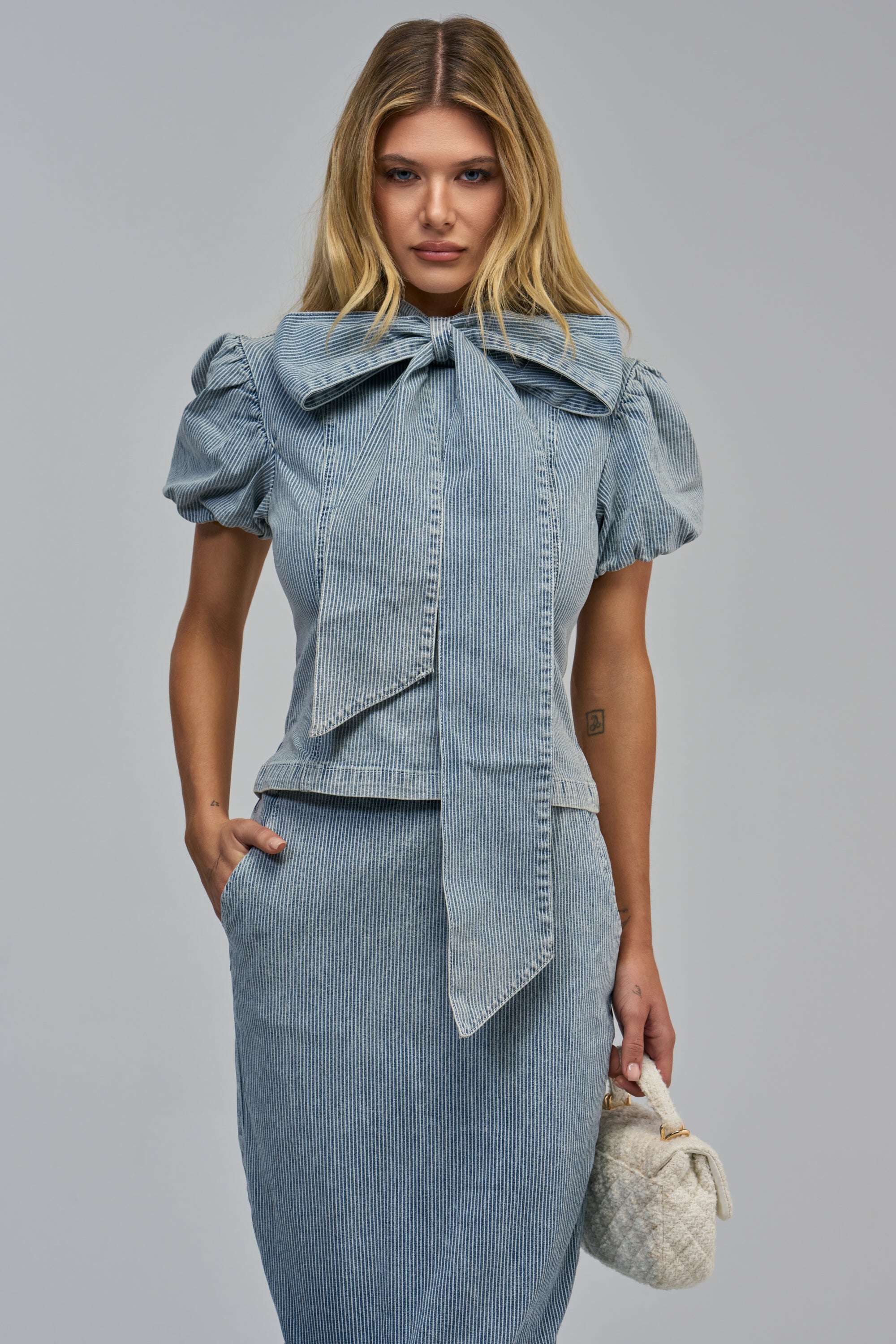 DENIM DEBUT SHORT SLEEVE BOW TOP featuring a short-sleeved pinstripe denim top with a large bow at the neckline and a matching skirt.
