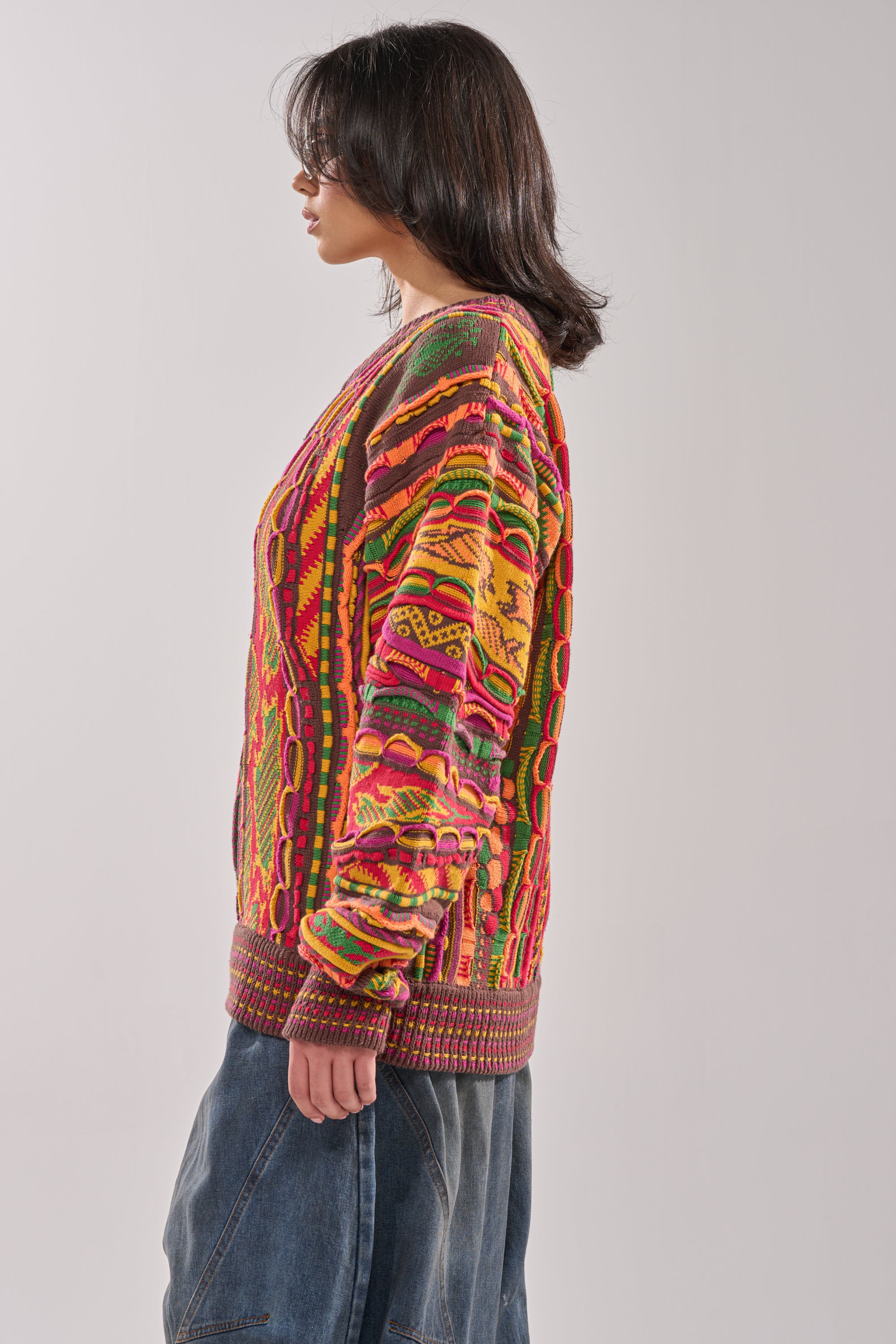 A person with shoulder-length dark hair, in profile against a plain light background, wears the THROWBACK SPECIAL KNIT SWEATER and loose blue jeans. 2
