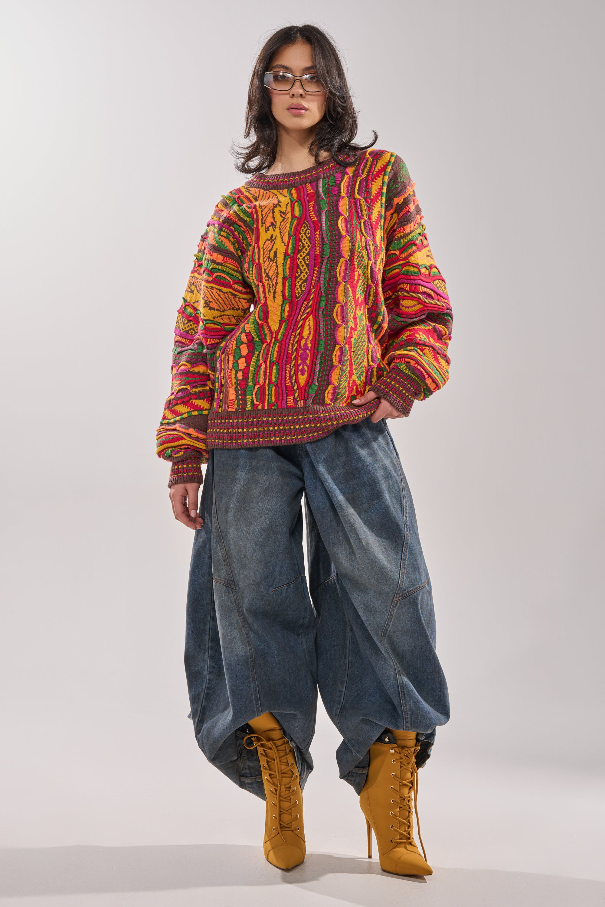 Wearing the THROWBACK SPECIAL KNIT SWEATER, oversized wide-leg jeans, yellow lace-up boots, and glasses, a person stands confidently against a plain light background. 4