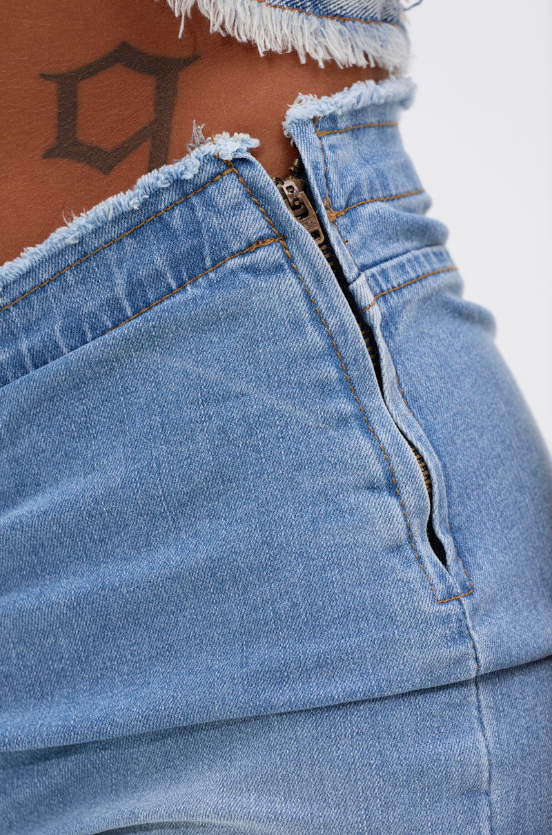 Close-up of a person wearing CINCHED UP SKINNY DENIM PANTS with a visible zipper and frayed waistband, revealing part of a geometric black tattoo above the denim. 6