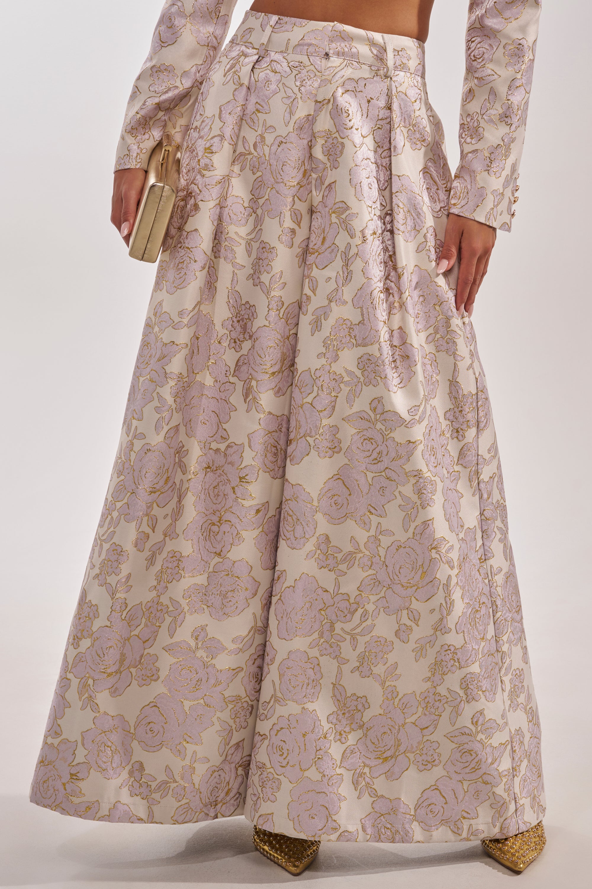 Wearing CHERI BROCADE WIDE LEG PANT featuring a pale pink and gold metallic floral print, paired with a matching long-sleeve top, gold clutch, and pointed gold shoes. 3