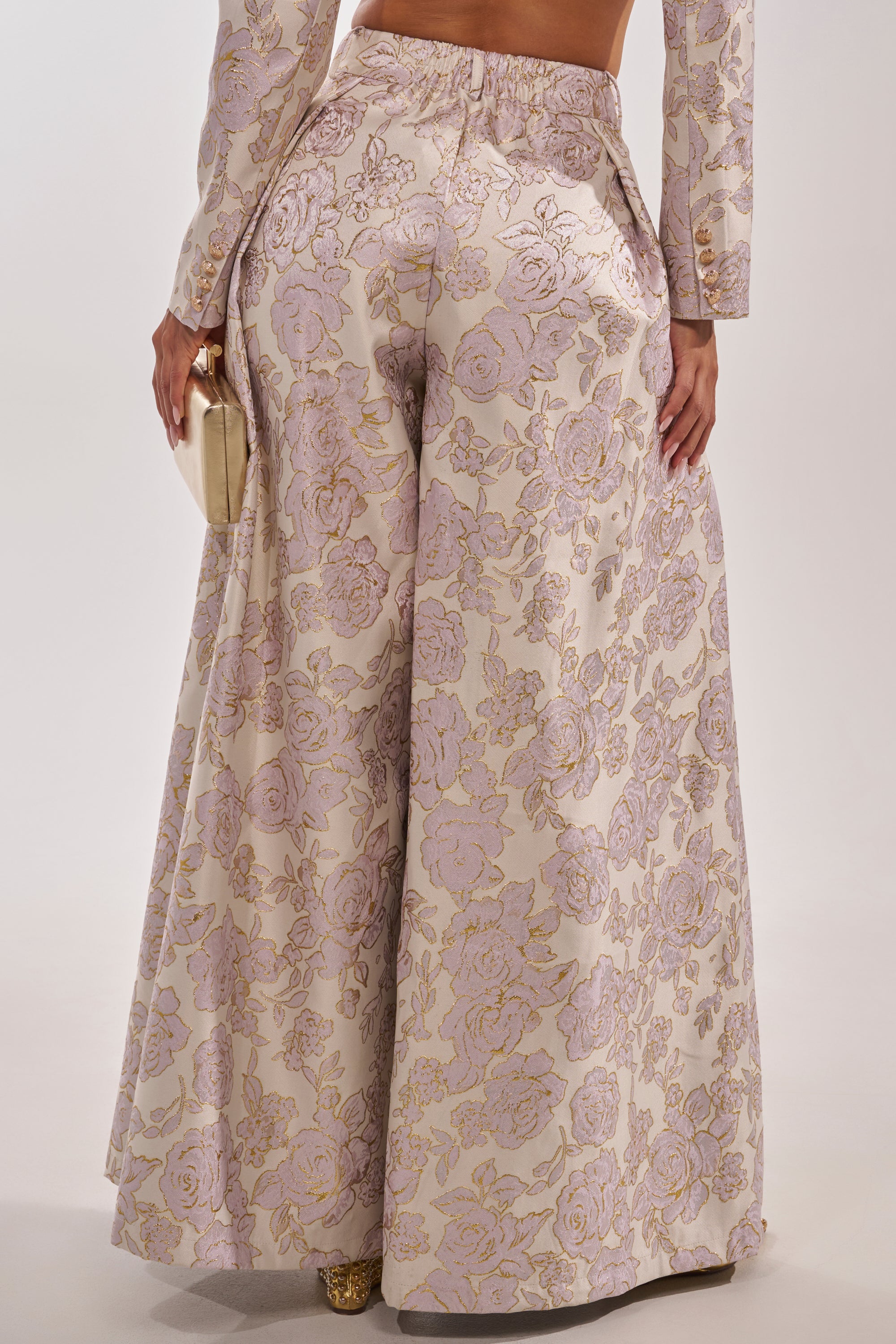 A person is seen from the back wearing the CHERI BROCADE WIDE LEG PANT with metallic light pink and gold floral detailing, accessorized with a gold clutch. 5
