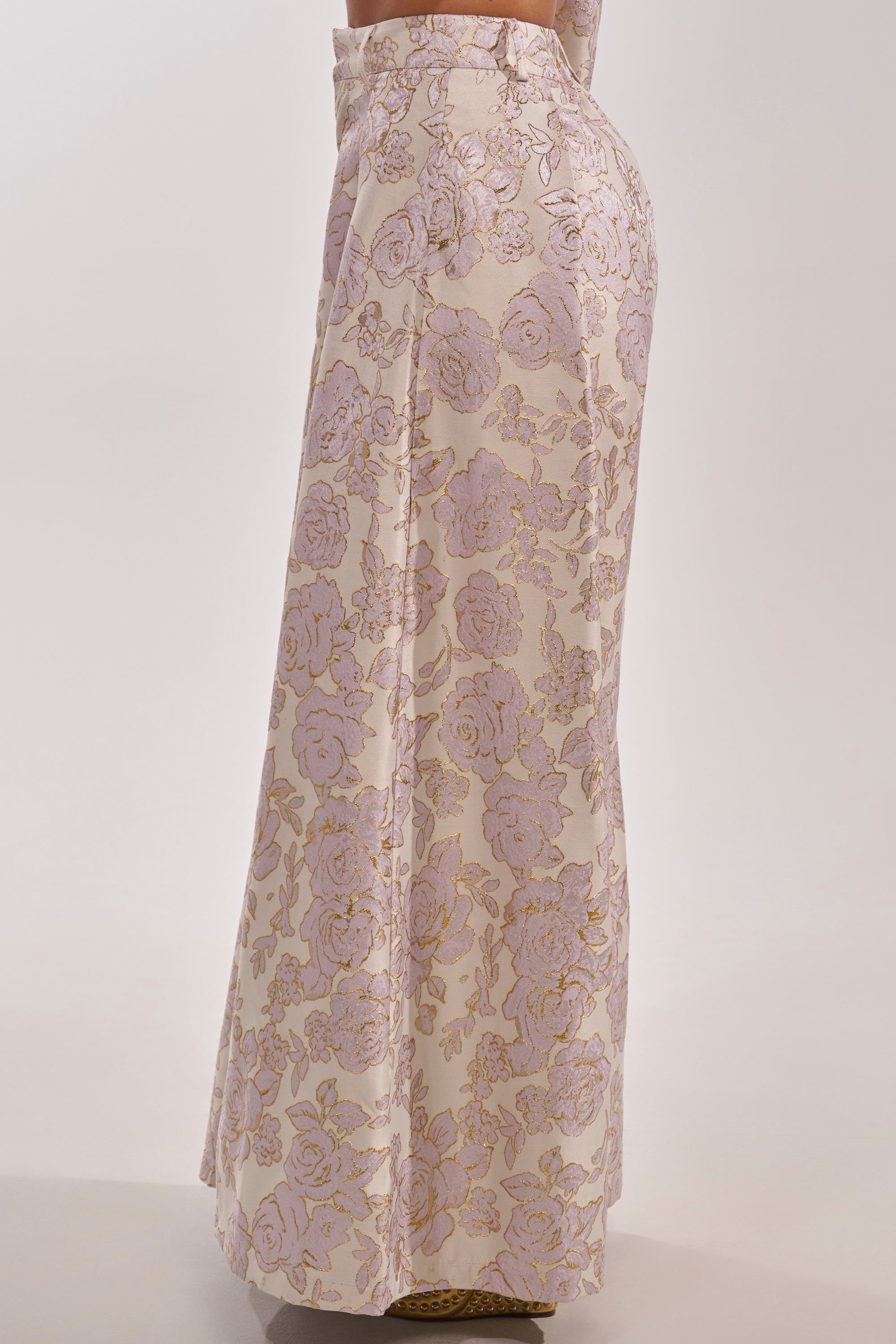 A person wearing the CHERI BROCADE WIDE LEG PANT, featuring a metallic pale pink and gold floral pattern, stands on a neutral background. 6