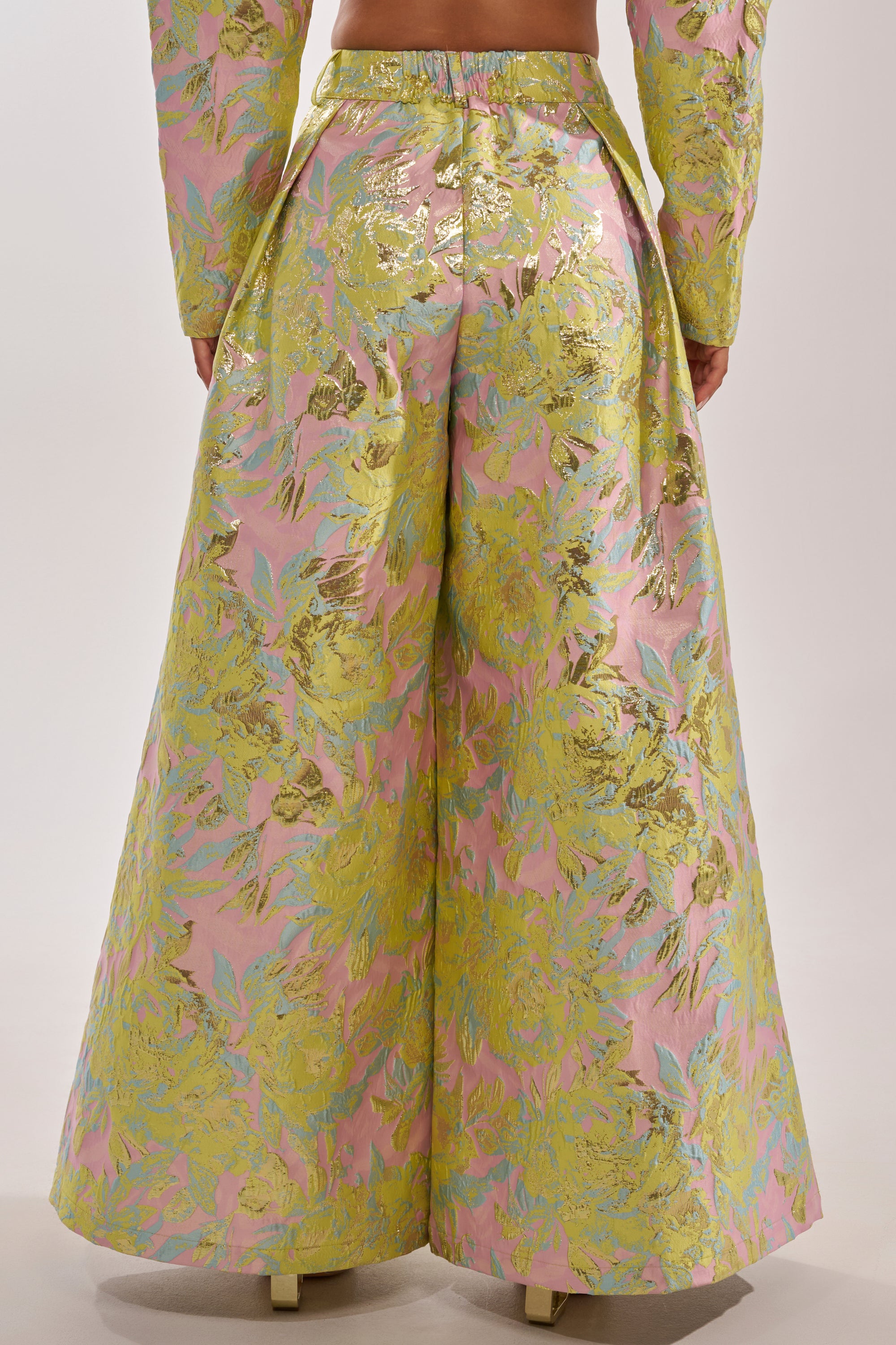 Someone photographed from the back is wearing the LUCY BROCADE WIDE LEG PANT in metallic brocade with an iridescent pink, yellow, and green floral pattern, paired with a matching long-sleeved top. 5