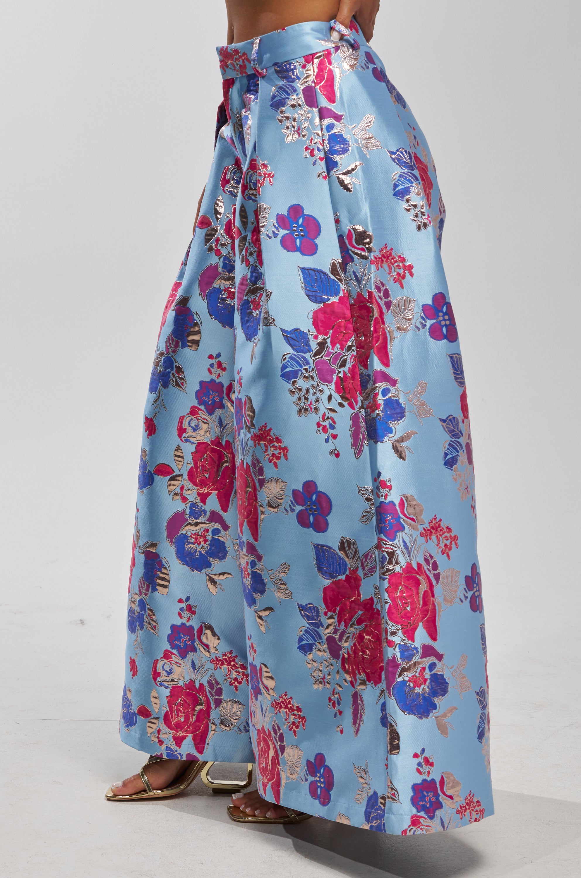 Someone styled the BUY MYSELF FLOWERS BROCADE TROUSER IN BLUE, featuring a shiny blue base with bold red, pink, and purple floral patterns, paired chicly with open-toe sandals.
