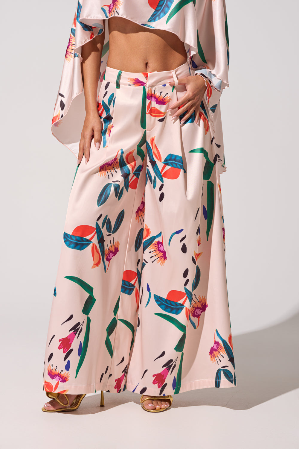 Wearing the CANDY RAIN SATIN WIDE LEG PANT in a vivid pink floral and abstract print, styled with gold heels and a matching crop top—an eye-catching choice for standout spring looks. 3