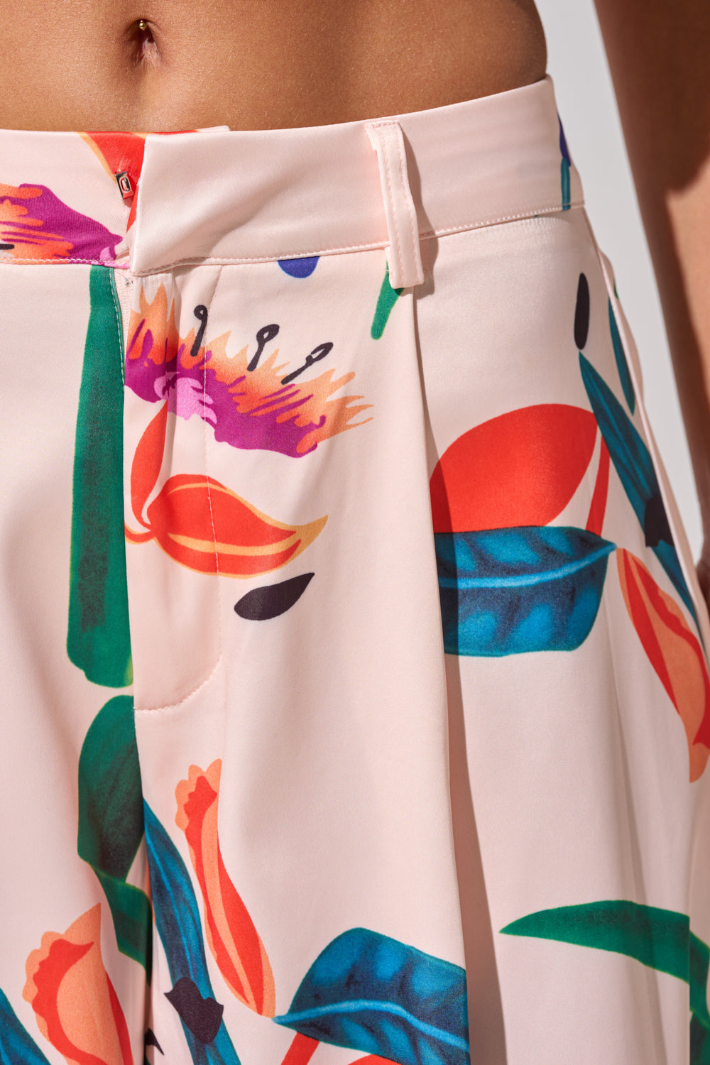Close-up of CANDY RAIN SATIN WIDE LEG PANT in light pink, featuring a colorful floral and leaf pattern, pleats, high waist, zipper fly, and wide legs. 7