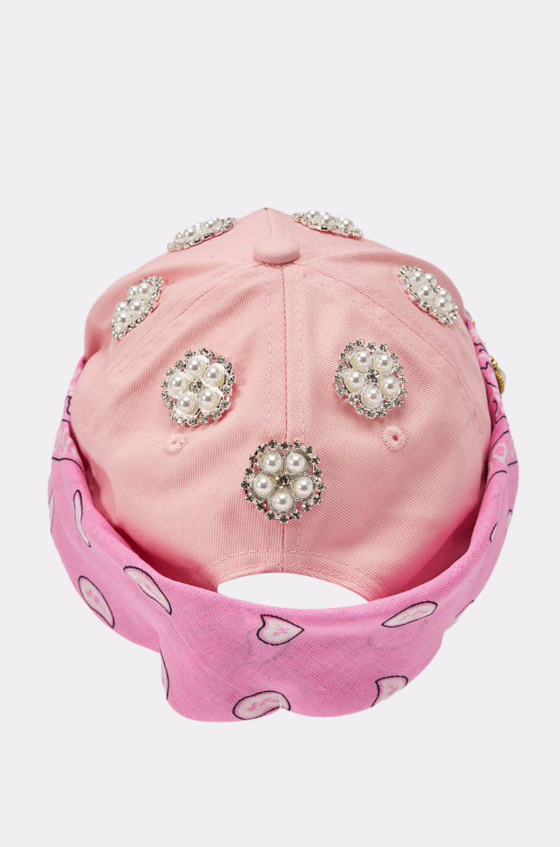 The ASTRA PAISLEY BROOCH HAT is a pink rhinestone hat with pearl and rhinestone floral embellishments, finished with a pink bandana featuring white and black paisley patterns for a chic bandana accent cap style. 3