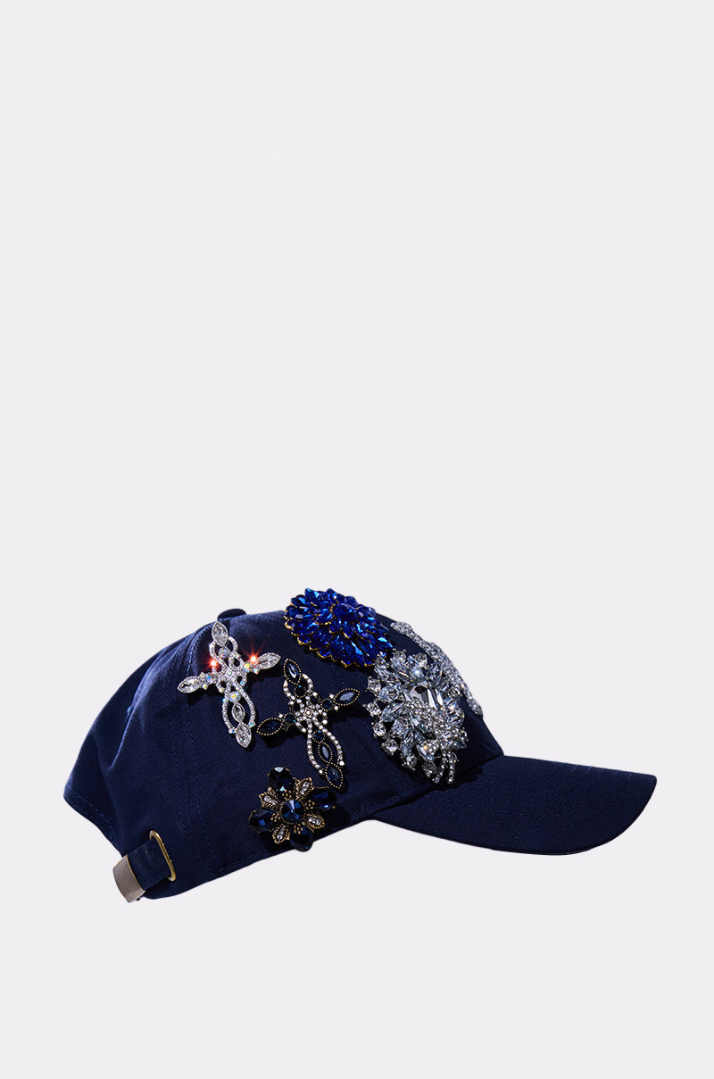 The IN THE NIGHT CHARM HAT is a navy blue baseball cap adorned with large, sparkling jeweled embellishments in silver, blue, and black on the side and top. 3