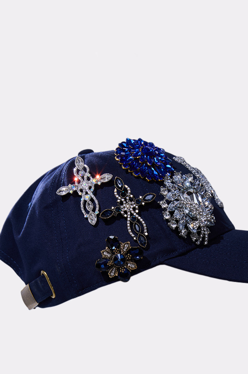 The IN THE NIGHT CHARM HAT is a navy blue baseball cap adorned with five jeweled brooches in silver, blue, and black, shown on a plain light background. 4