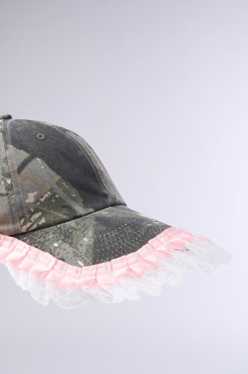 The GIRLY VIBES CAMO HAT is a stylish baseball cap featuring camo print and a pink ruffled lace trim, shown against a plain light gray background.