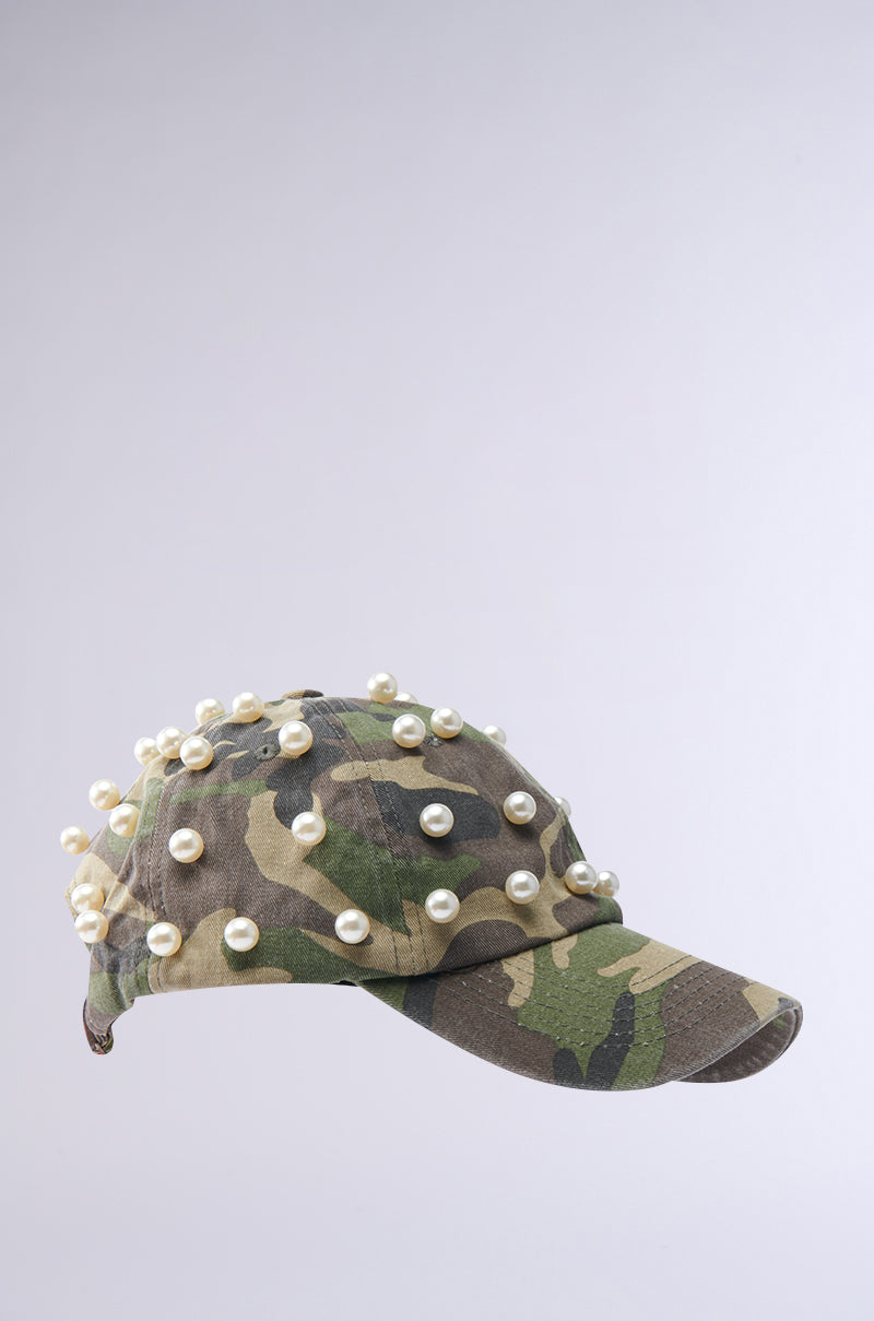 The PEARL PLEASE CAMO HAT showcases a classic camouflage print topped with multiple white pearl accents, set against a plain light gray background. 3