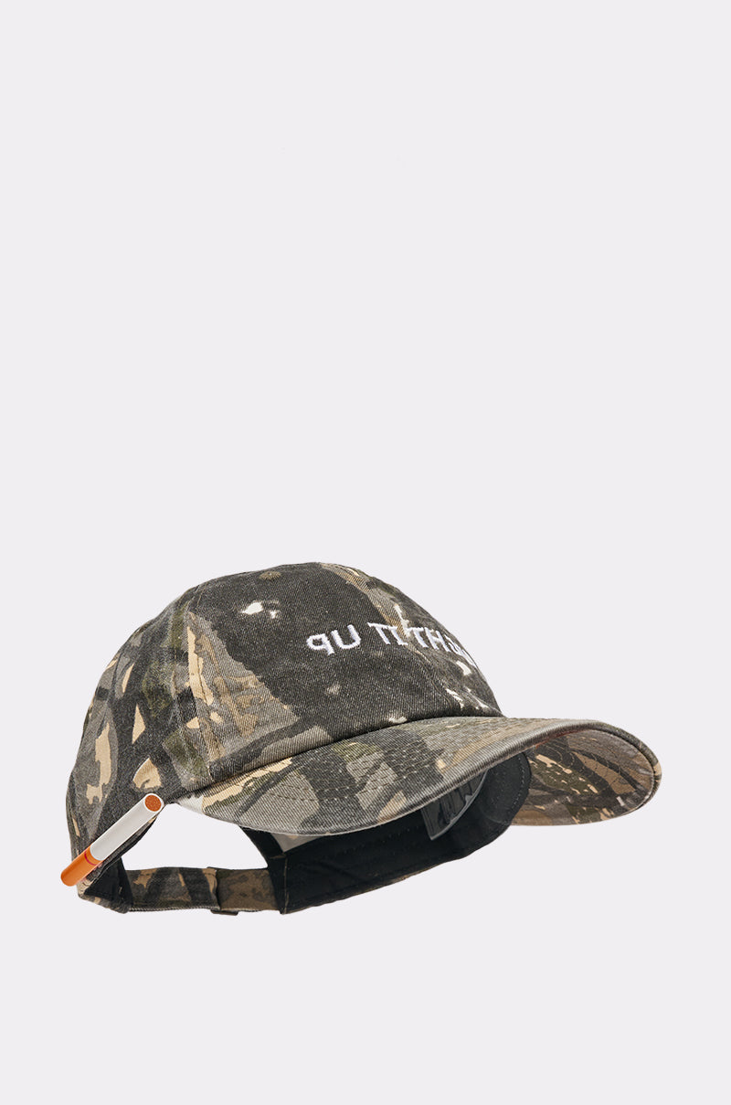 The LIGHT IT UP FAUX CIG HAT is a camo baseball cap with an adjustable strap and metal buckle. The front features partially visible white text that appears to say “LIGHT IT UP,” adding a street style edge. 5