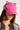 A person wearing a hot pink TOO COI SNAPBACK embellished with cat ears and small rhinestones. The individual has long brown hair and is dressed in a black outfit with gold accents. The person's face is partially visible, and they are looking slightly downward.