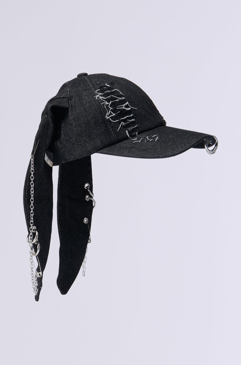 The AERIAL VIEWS HAT is a black denim cap featuring distressed stitching, adorned with metallic silver elements such as metal studs and chains that hang from the brim and sides. It also includes unique fabric extensions that enhance its edgy, avant-garde style. 3