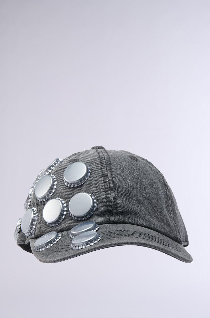 The BOTTLES ON ME HAT from AKIRA Label is a dark gray baseball cap with bold bottle cap accents on the front and side, displayed against a solid light gray background.