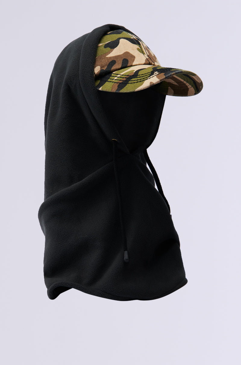 The BROOKLYN CAP AND HOOD, featuring a camouflage pattern baseball hat, is subtly hidden beneath a green hooded garment, creating a fashionable layered appearance against a simple backdrop.