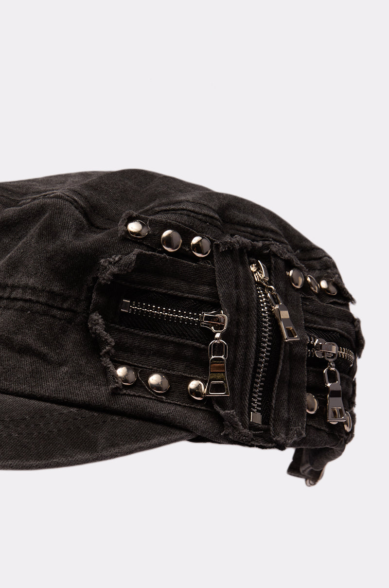 A close-up of the I REALLY DO THIS HAT, a punk-rock cap made from black distressed denim with zippers, metal studs, and frayed details, shown against a plain light background. 5