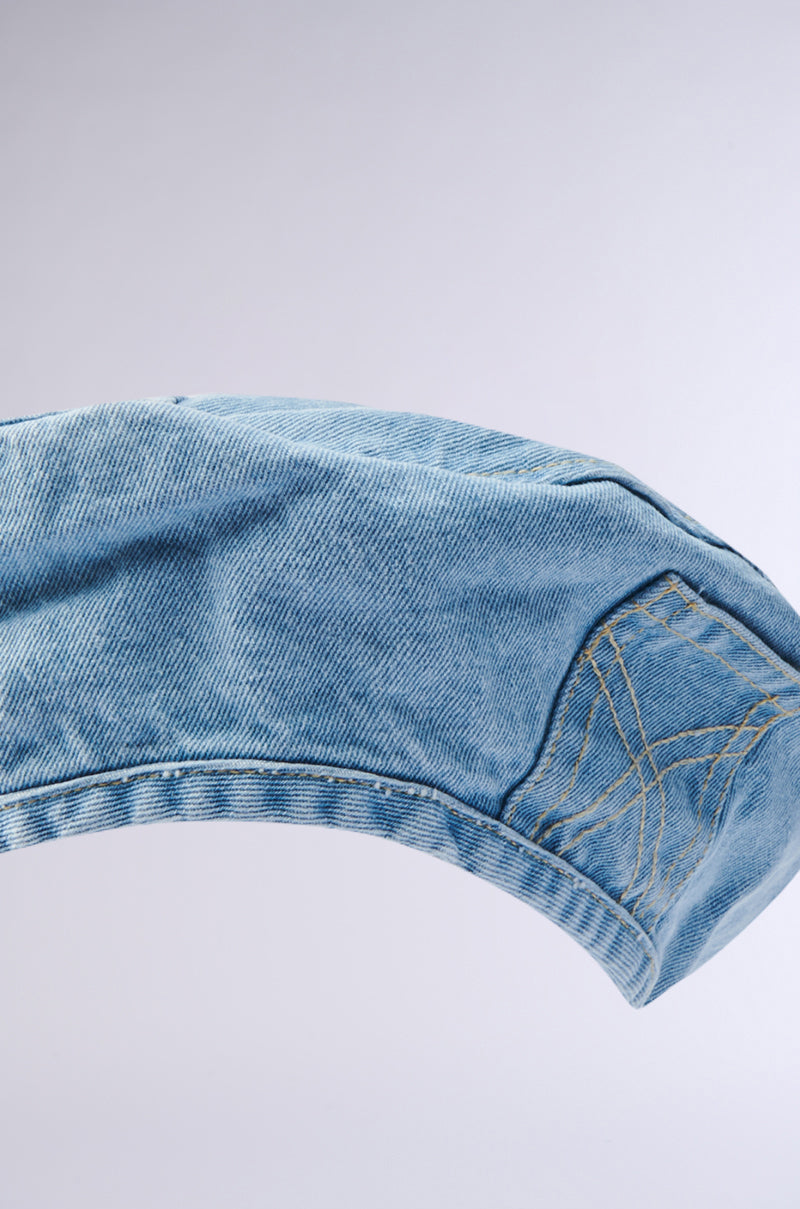 A close-up of light blue denim jeans’ curved edge, detailed stitching, and seams stands out against a pale background—a look that pairs perfectly with a chic accessory like the IT GURL DENIM BERET.
