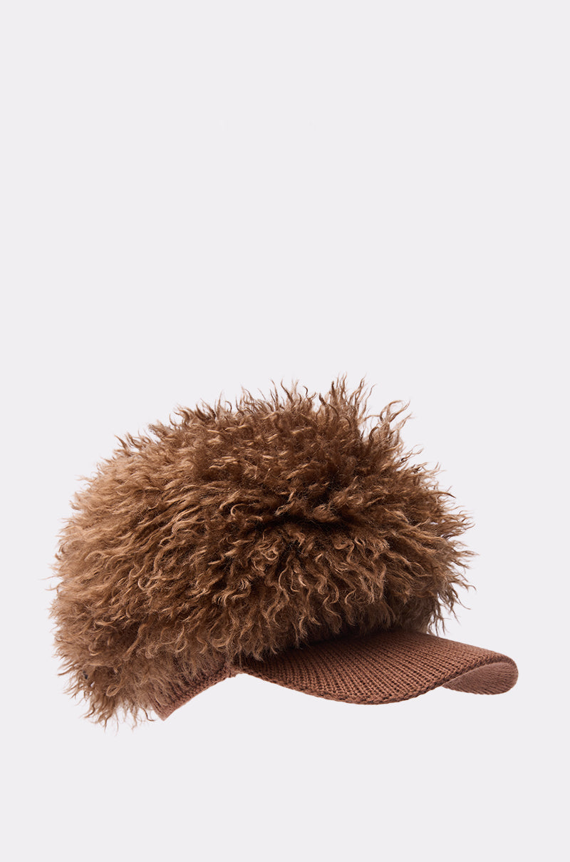 The WHOS HAIR HAT is a brown baseball cap featuring a large, fluffy, curly-textured faux fur top, shown against a plain light background.