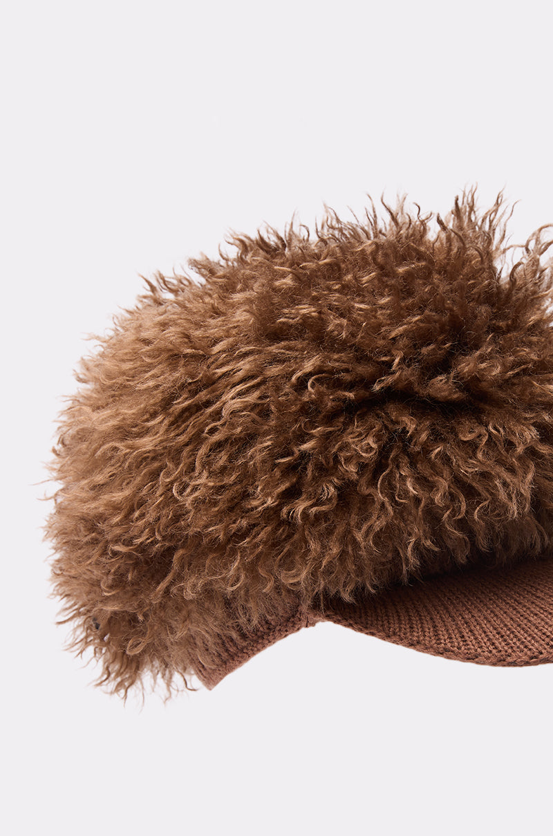 A brown WHOS HAIR HAT by AKIRA Label, featuring a large fluffy curly faux fur top, displayed against a plain light backdrop.