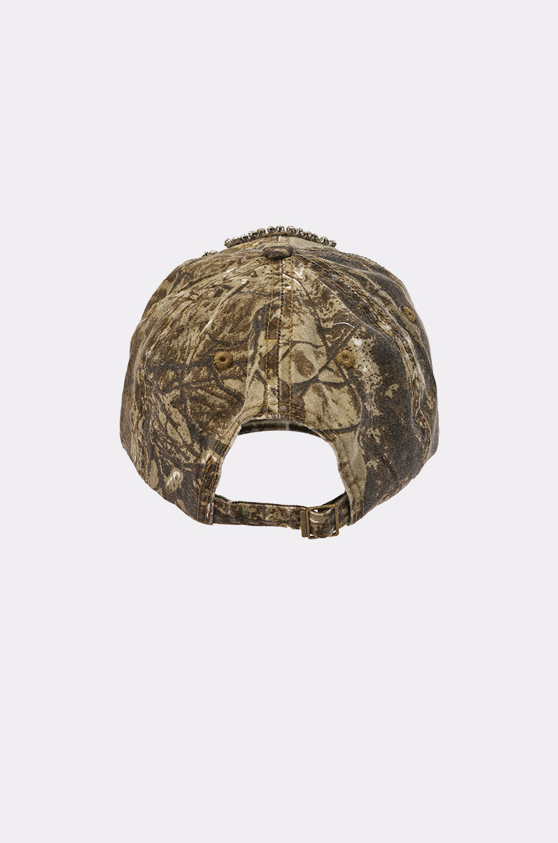 The SEE ME APPLIQUE HAT is a camo baseball cap in earthy brown and green tones, shown from the back with an adjustable strap and buckle, set against a plain white background. 5
