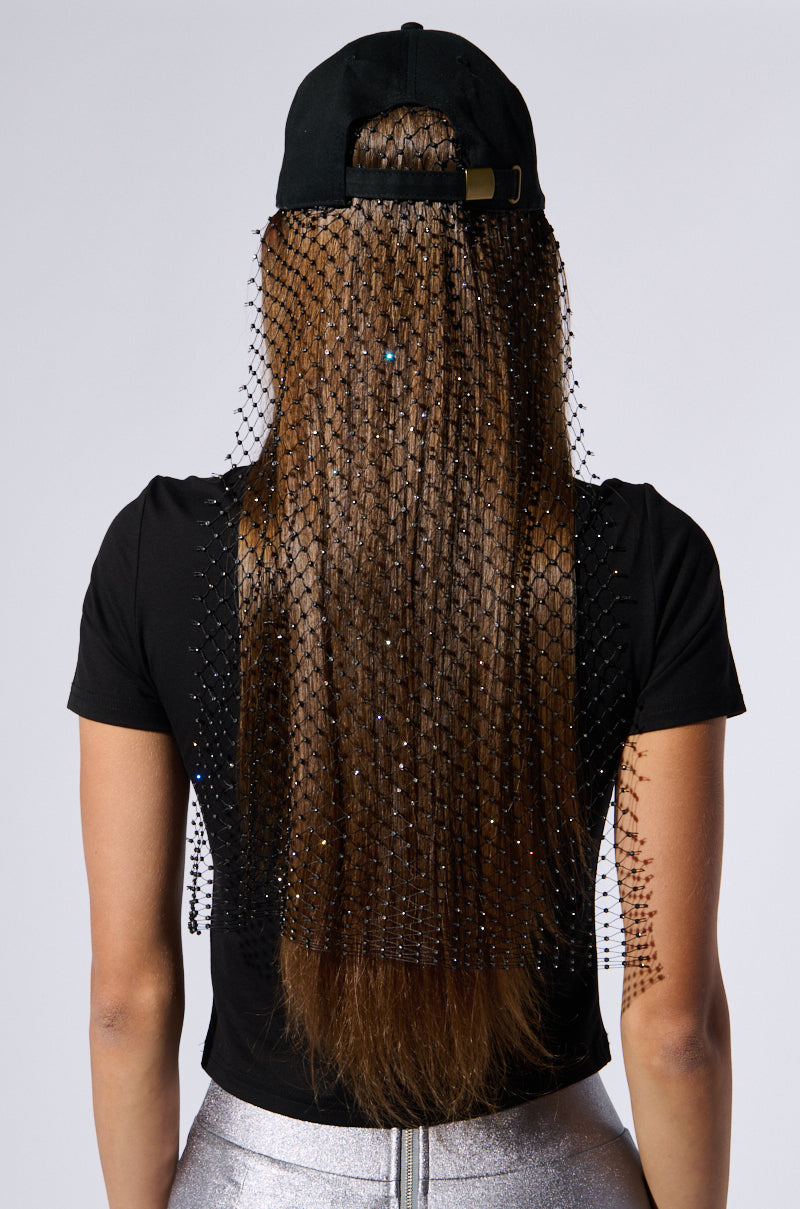A person with long, straight brown hair is photographed from the back. They are wearing the "PROUD OF ME RHINESTONE SNAPBACK" featuring a decorative black net covering their hair, a black t-shirt, and metallic silver pants. The background is plain light gray. 1