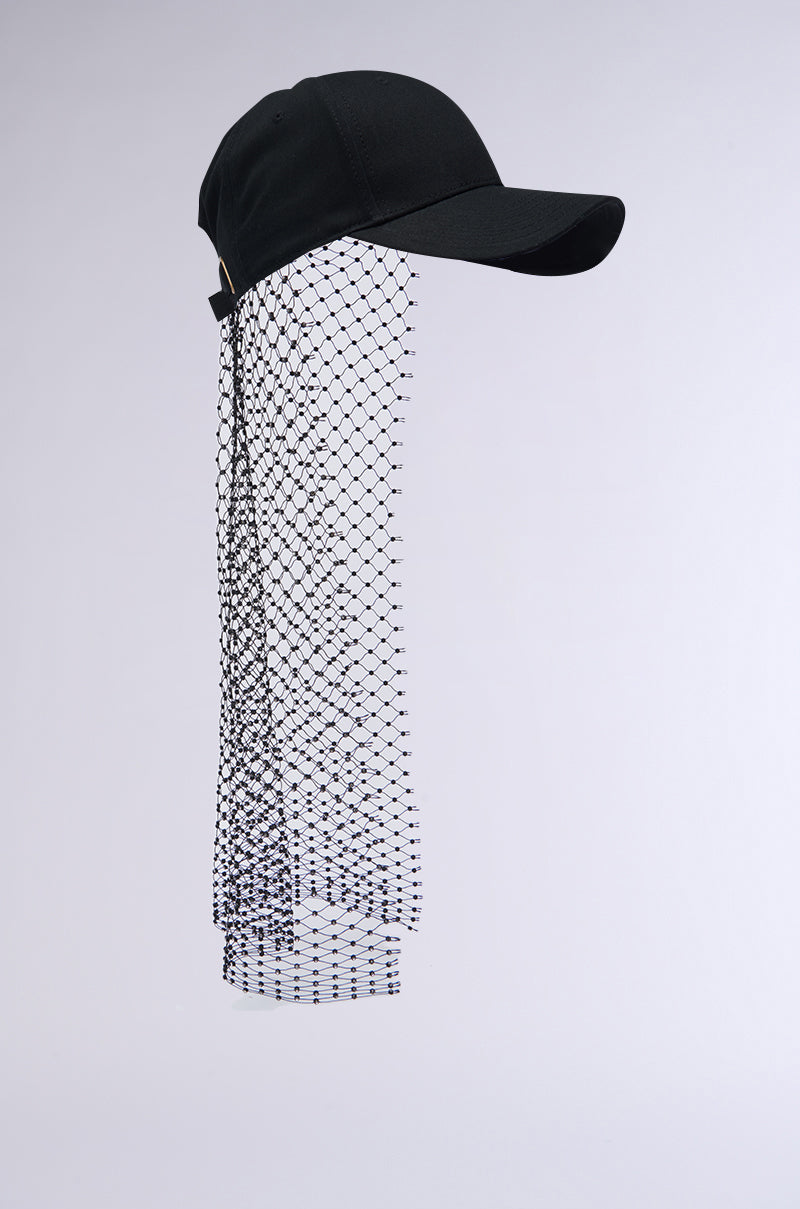 The PROUD OF ME RHINESTONE SNAPBACK is a black baseball cap with an attached fishnet mesh veil that hangs down to shoulder length against a plain white background. The veil features a diamond pattern, creating an interesting contrast with the solid fabric of this adjustable strap cap. 3