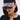 A woman wears the NAILED IT HAT, a black ball cap decorated with pink and black press-on nail accents on the brim, styled with oversized sunglasses and a black lace-trim buttoned top.
