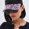 A woman wears the NAILED IT HAT, a black ball cap decorated with pink and black press-on nail accents on the brim, styled with oversized sunglasses and a black lace-trim buttoned top.
