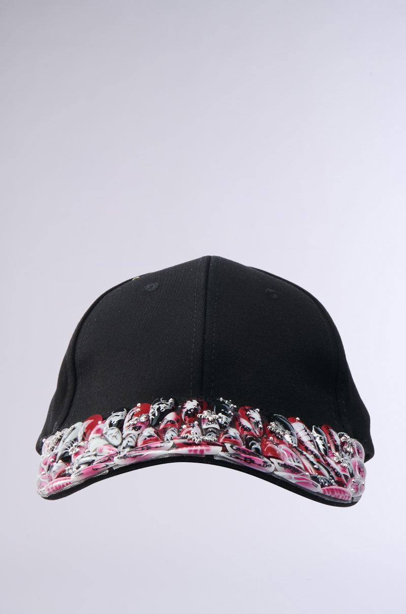 The NAILED IT HAT is a black ball cap with a vibrant abstract red, pink, white, and black patterned brim, shown against a plain light gray background.