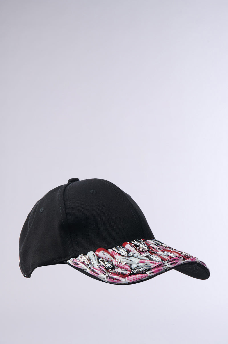The NAILED IT HAT is a black ball cap showcasing a graphic design of red, white, and gray lipstick tubes on the brim, set against a plain light background.