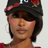A person wearing the BIG CITY BROOCH TRUCKER HAT, which features "NYC" embroidery and is embellished with red and pink floral patches. They have hoop earrings, a red top, a chunky chain necklace, and are accessorized with sparkling rhinestone brooches.