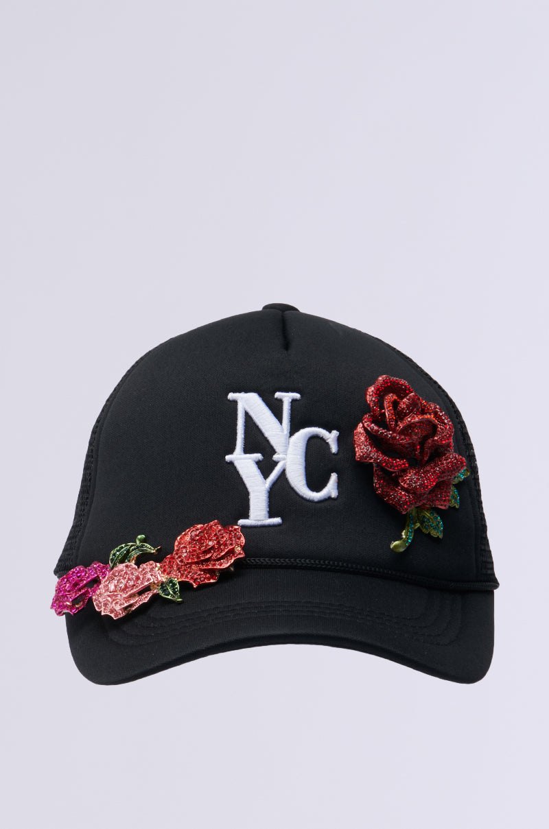Introducing the BIG CITY BROOCH TRUCKER HAT: a black cap featuring "NYC" embroidered in white on the front, complemented by decorative red and pink roses along the brim and side for a chic floral touch.