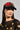 A woman wearing the "WITH LOVE PATCH SNAPBACK," a black hat featuring red and gold embroidered heart designs, complemented by her large hoop earrings. She has straight hair and is dressed in a black mesh top adorned with gold embellishments.