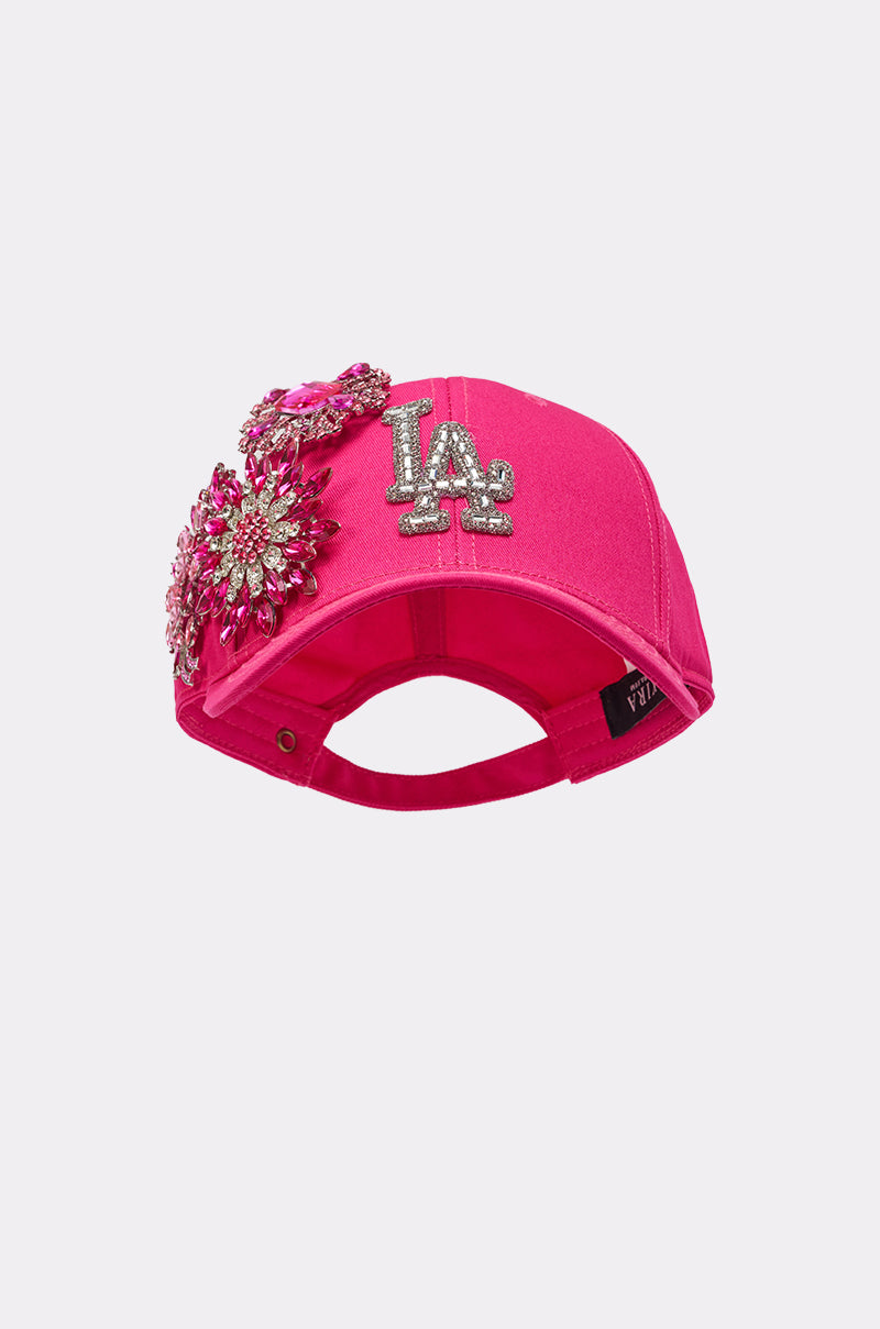 The VAL BROOCH HAT is a hot pink baseball cap with a rhinestone LA logo and sparkling crystal floral appliqués, including jeweled logos and decorative side designs. 1