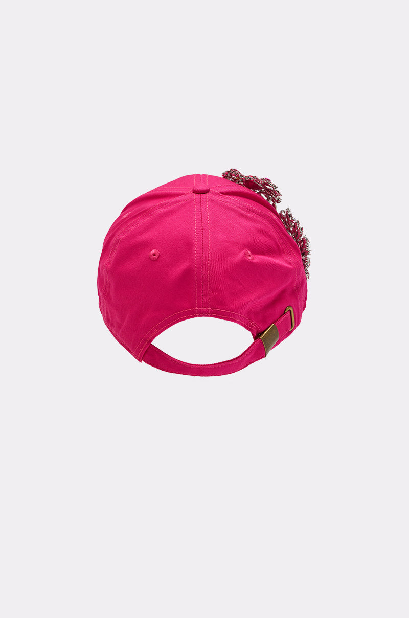 The VAL BROOCH HAT is a hot pink baseball cap shown from the back, featuring an adjustable strap with a metal clasp and crystal floral appliqués on the side for extra flair. 3