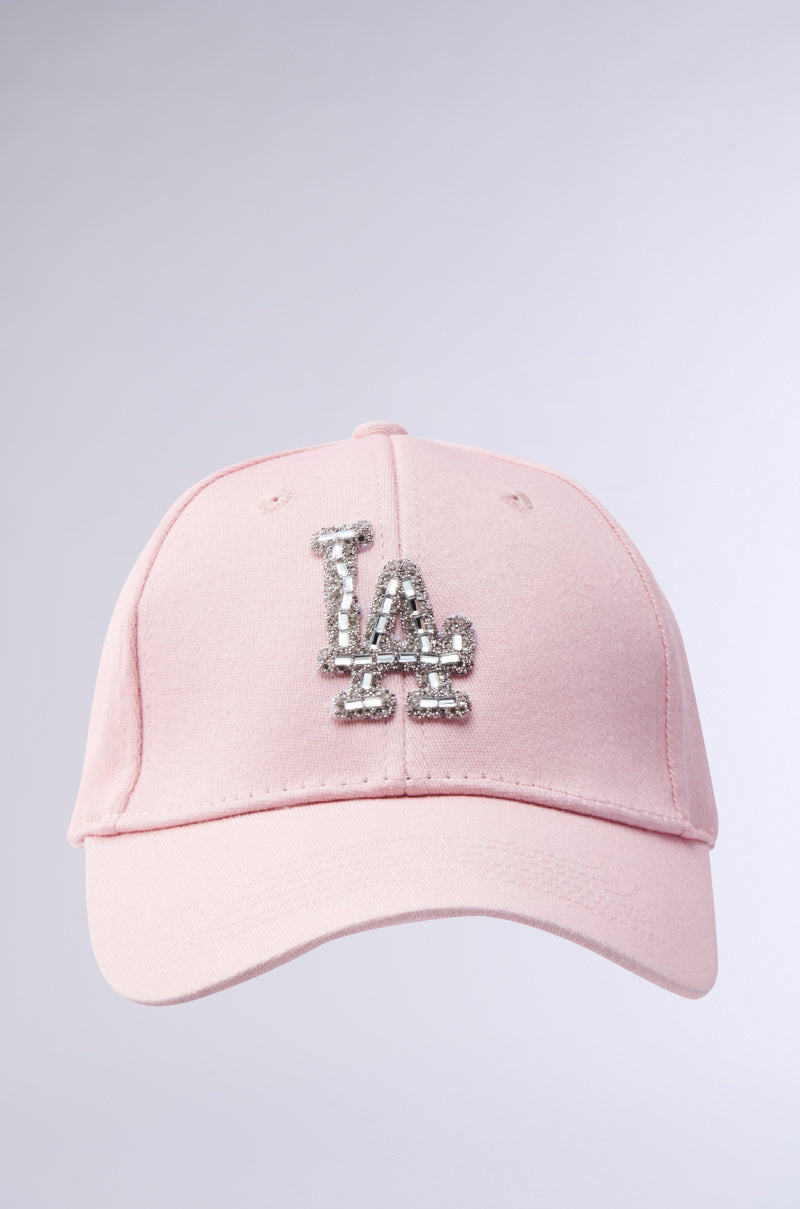 The CATCH FLIGHTS HAT is a light pink baseball cap with a silver glittery "LA" logo on the front, shown against a plain light background.