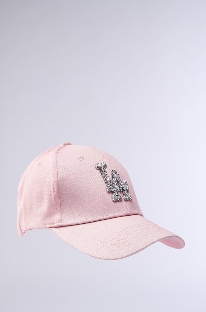 The CATCH FLIGHTS HAT is a light pink baseball cap with a curved brim and a glittery silver "LA" logo on the front, shown against a plain light background.