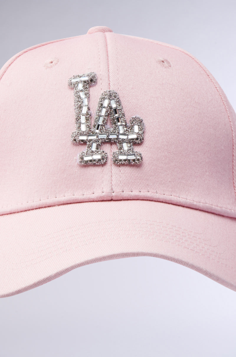 The CATCH FLIGHTS HAT is a light pink baseball cap with a sparkling rhinestone-embellished "LA" logo on the front.