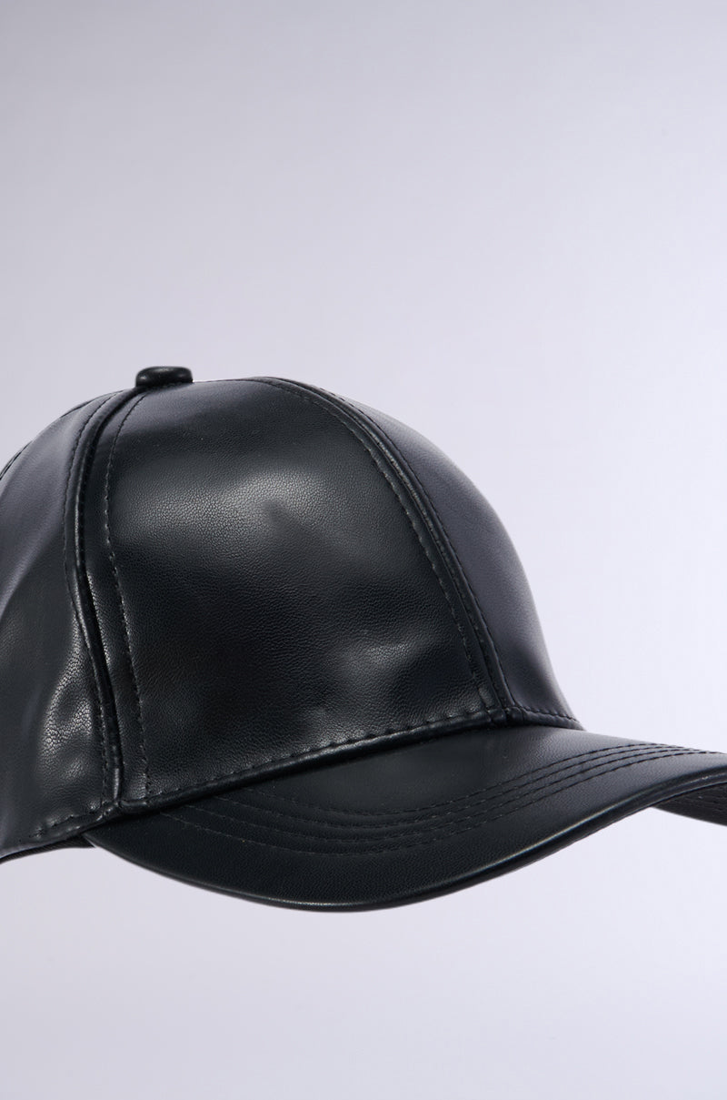 The PU SNAPBACK is showcased against a plain gray background. The black faux leather cap features a smooth, glossy finish with visible stitching along the panels and brim, contributing a subtle texture to its sleek design. An adjustable strap ensures it provides a perfect fit for any head size. 4