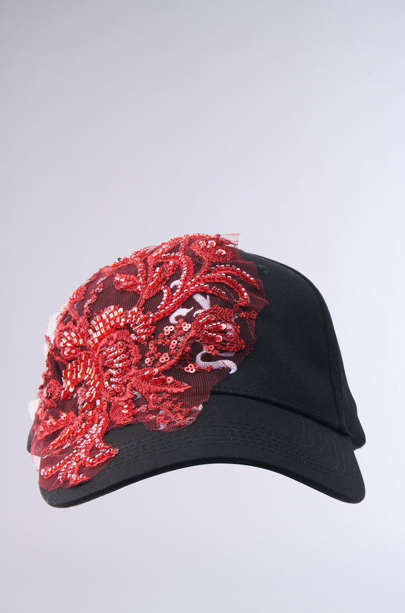 The IN MY CITY APPLIQUE HAT is a black baseball cap with an ornate red floral sequin and bead design on the left front panel, displayed against a plain light gray background.