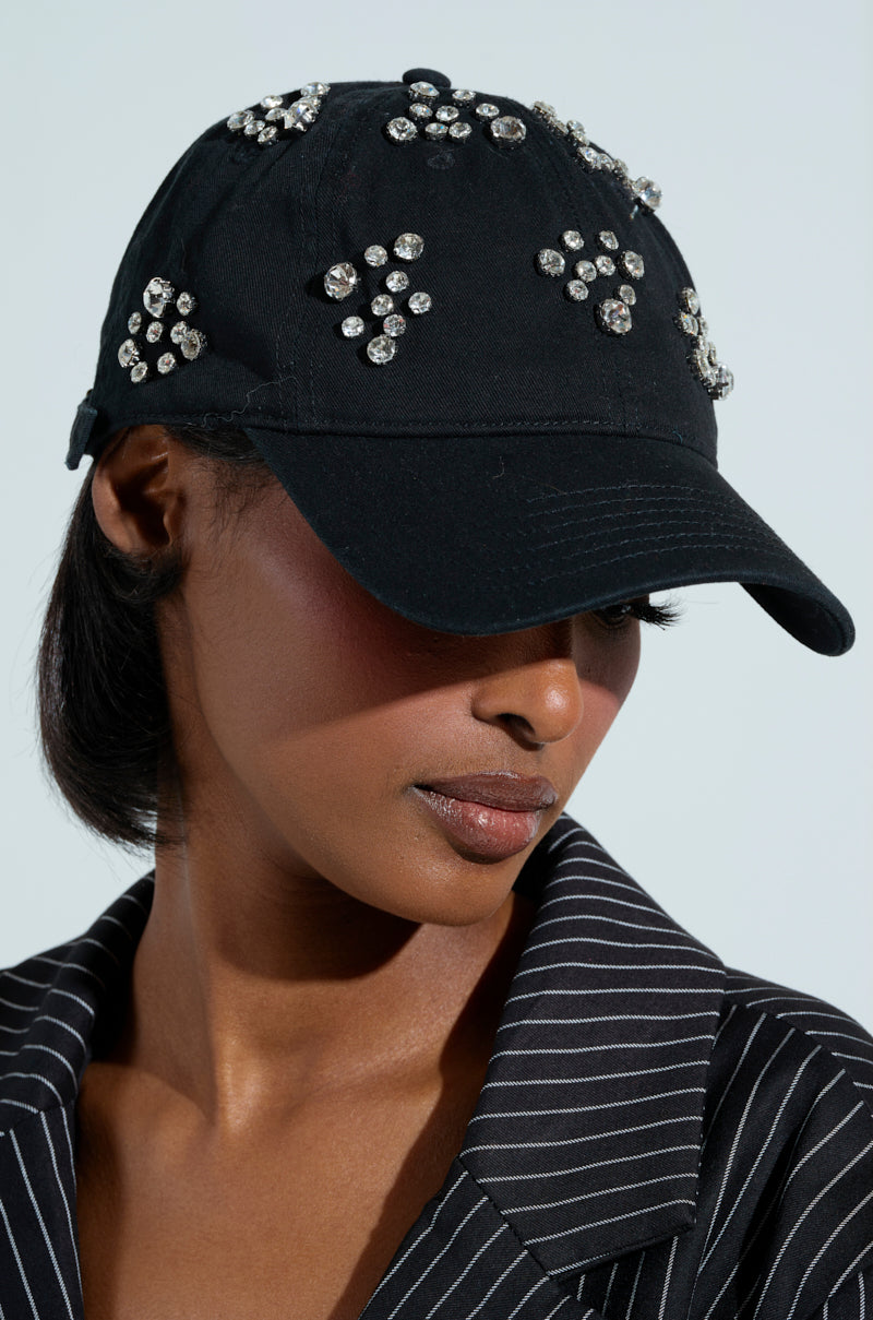 Wearing the TO THE GRAM RHINESTONE HAT with an adjustable strap and a black pinstripe blazer, a person gazes downward against a softly blurred background.