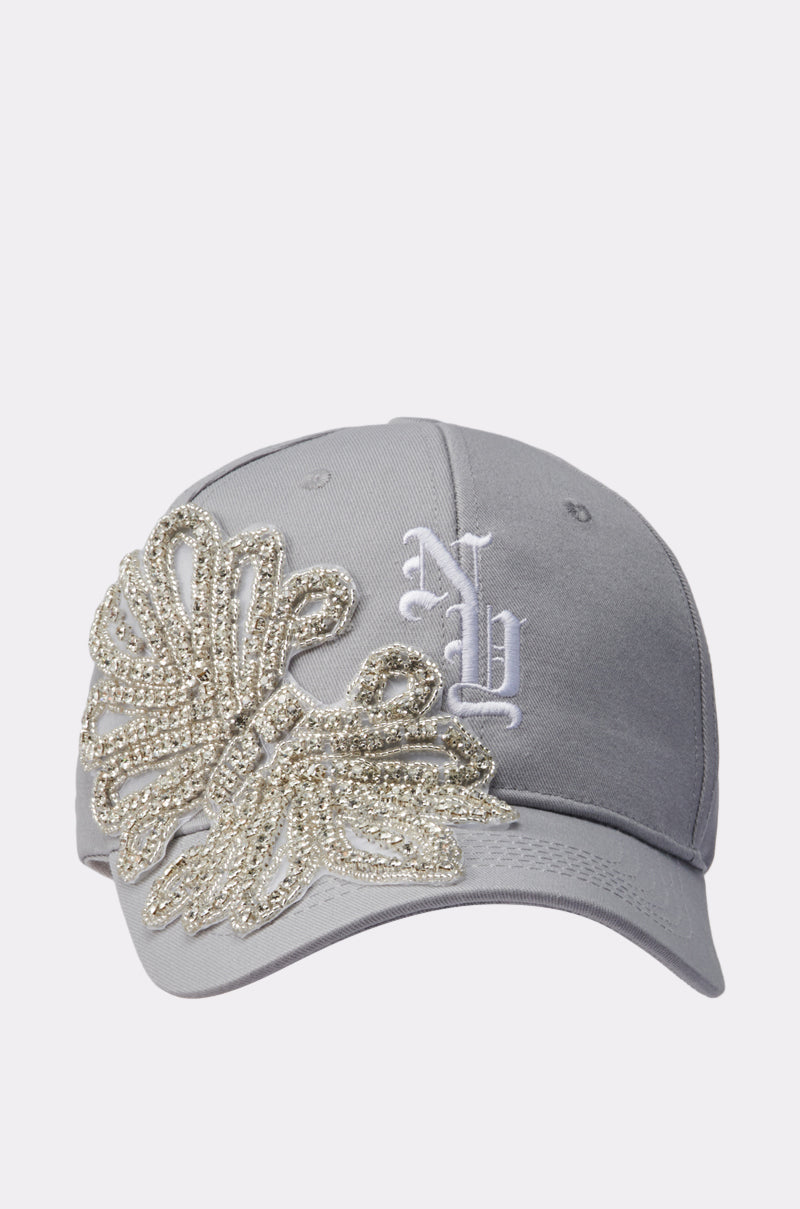 The IM TOO GOOD APPLIQUE HAT is a gray AKIRA Label baseball cap with a white embroidered "NY" logo and an eye-catching gold and silver beaded applique on the front left side.