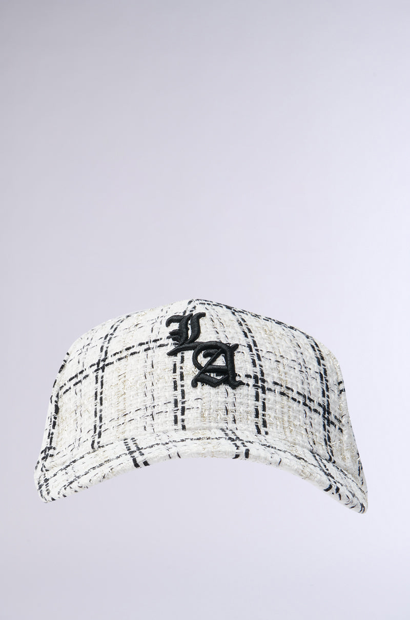 The COME TO ME HAT, a white tweed baseball cap with a black checkered pattern and bold LA embroidery on the front, crafted from premium tweed, is shown against a light gray background. 1