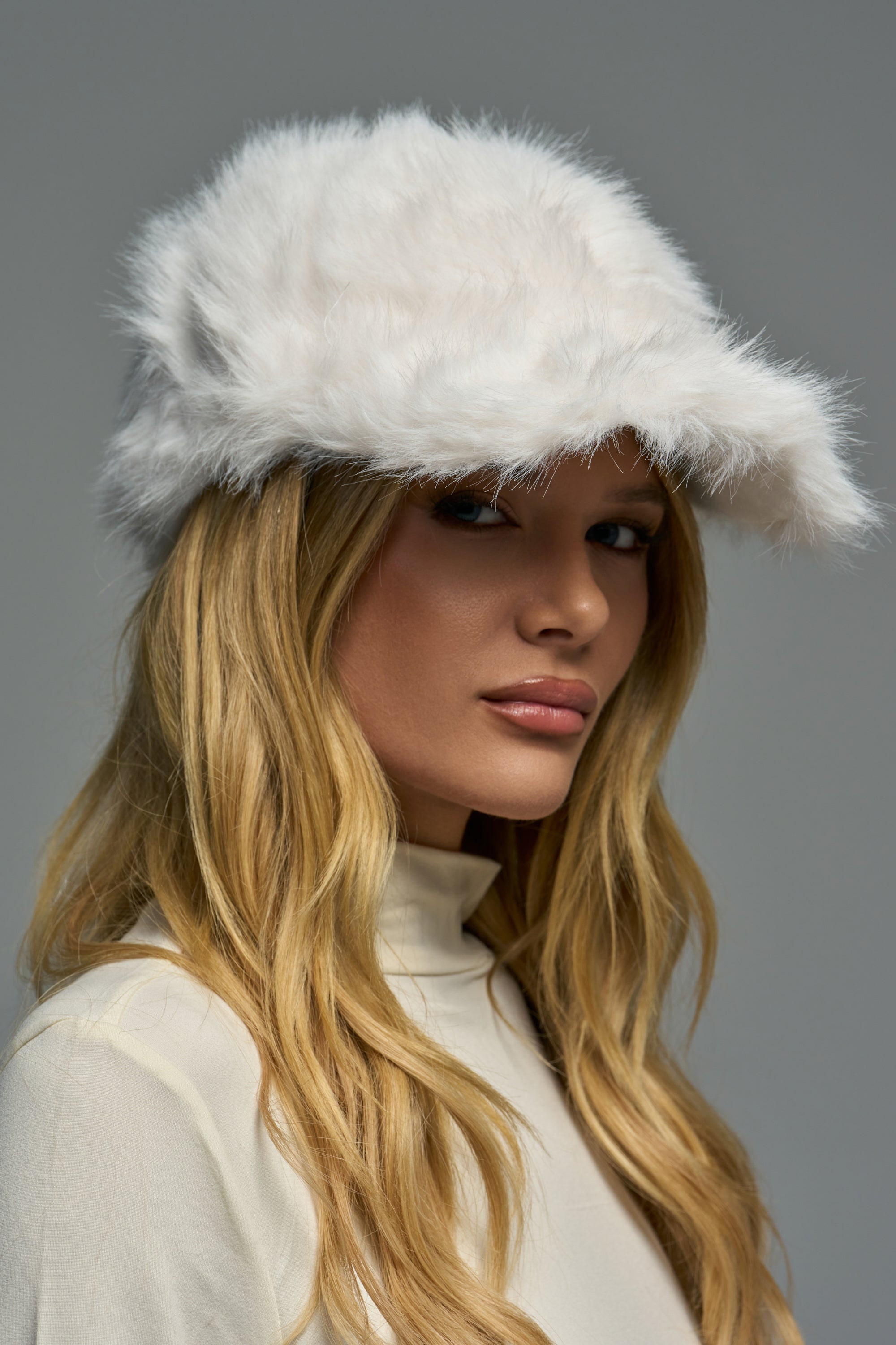 A person wears a white faux fur WHITE FUR BASEBALL CAP for cold weather styling.