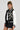 A person dressed confidently in a chic black and white DRAGONETTE EMBELLISHED BOMBER, adorned with intricate dragon motifs, exudes style. They complement their look with braided hair, sunglasses, a crisp white shirt, and a sleek black skirt against a plain backdrop that enhances their fashion-forward ensemble.