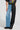 A person wearing the distinctive Extreme Stretch Patchwork Wide Leg Jeans makes a bold fashion statement by combining one side with light blue denim and the other with black leather-like material, perfectly paired with black shoes and a graphic T-shirt.